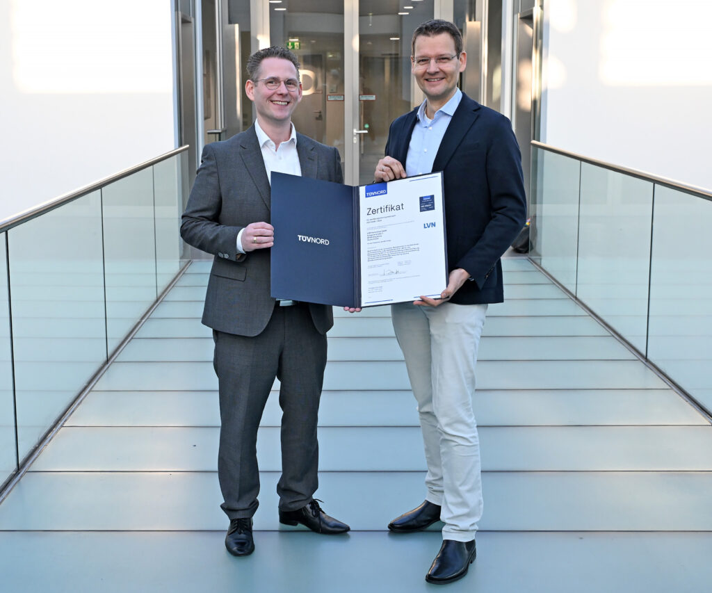 Tobias van Hasselt vom TÜV NORD (l.) übergibt das ISO 55001:2024-Zertifikat für die LVN an LEW-Vorstandsmitglied Malte Sunderkötter. (Bild: LEW, Jörg Mettlach)
