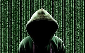 Hacker mit Hoodie sitzt vor einer Wand aus Code